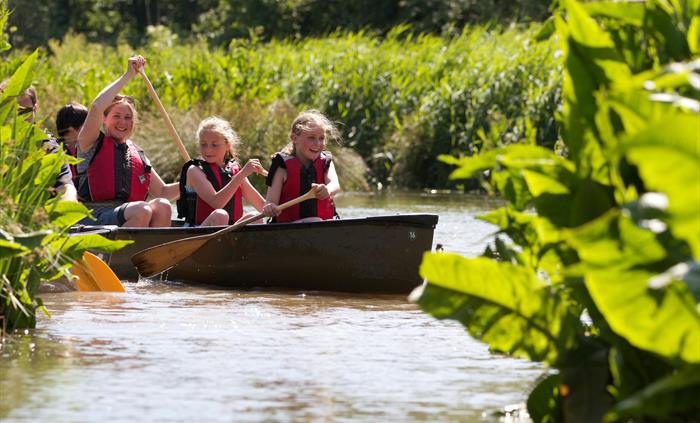 A family canoes around the waterways of WWT Llanelli's summer Canoe Safari